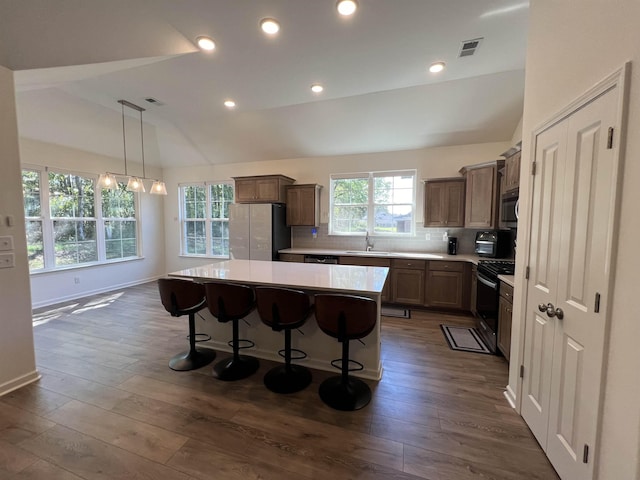 kitchen with pendant lighting, backsplash, vaulted ceiling, appliances with stainless steel finishes, and a kitchen island