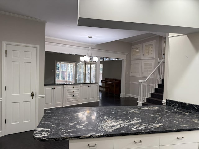 kitchen featuring pendant lighting, dark stone counters, white cabinets, ornamental molding, and a notable chandelier