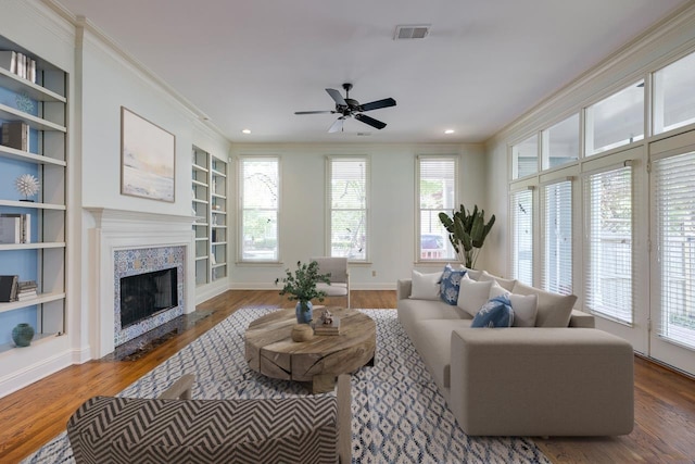 living room with a tiled fireplace, crown molding, built in features, and dark hardwood / wood-style floors