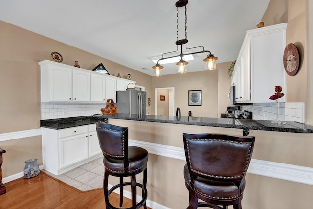 kitchen with white cabinetry, hanging light fixtures, stainless steel appliances, decorative backsplash, and light wood-type flooring