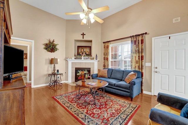 living room with hardwood / wood-style flooring, ceiling fan, a towering ceiling, and a fireplace