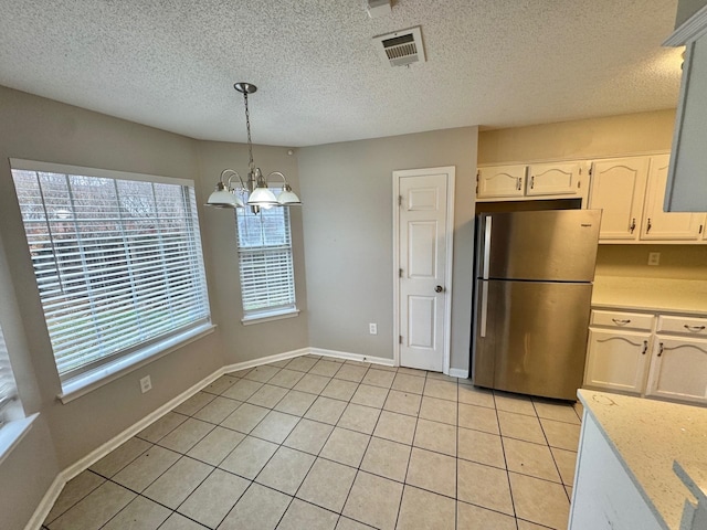 kitchen featuring pendant lighting, white cabinets, stainless steel fridge, light tile patterned floors, and a notable chandelier