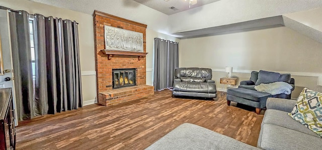 living room with ceiling fan, hardwood / wood-style floors, a textured ceiling, and a brick fireplace