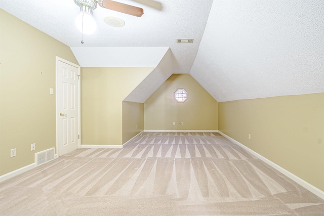 bonus room with lofted ceiling, ceiling fan, light colored carpet, and a textured ceiling