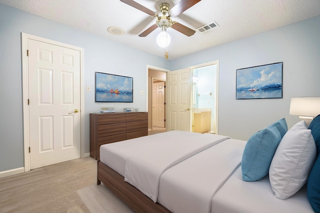 carpeted bedroom featuring a textured ceiling, ensuite bath, and ceiling fan