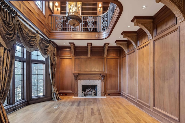 unfurnished living room with a tile fireplace, crown molding, a towering ceiling, light hardwood / wood-style floors, and wooden walls