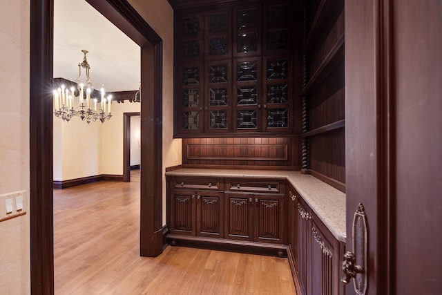 bar with decorative light fixtures, dark brown cabinetry, light hardwood / wood-style flooring, and an inviting chandelier