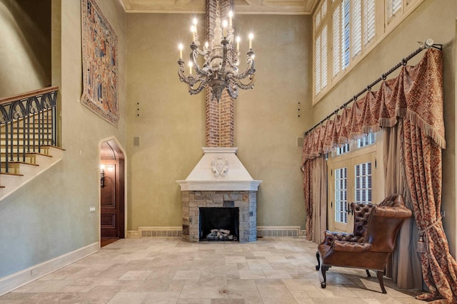 living area with a stone fireplace, a towering ceiling, a notable chandelier, and ornamental molding