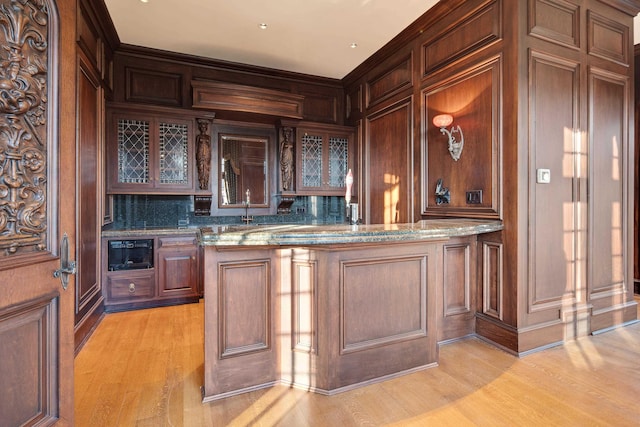 bar featuring dark brown cabinets, light hardwood / wood-style flooring, light stone counters, and sink