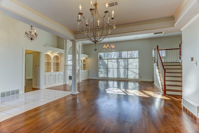 interior space with ornate columns, built in shelves, a raised ceiling, crown molding, and hardwood / wood-style flooring