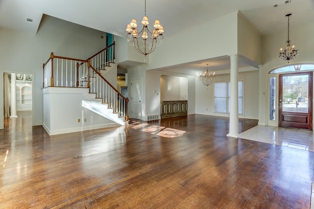 foyer featuring decorative columns, a towering ceiling, dark wood-type flooring, and a notable chandelier