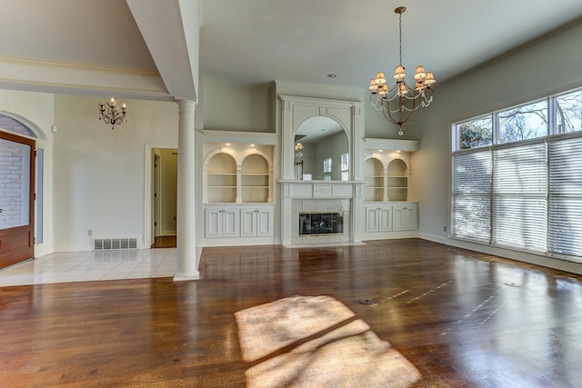 unfurnished living room featuring ornate columns, built in features, a tile fireplace, and a chandelier