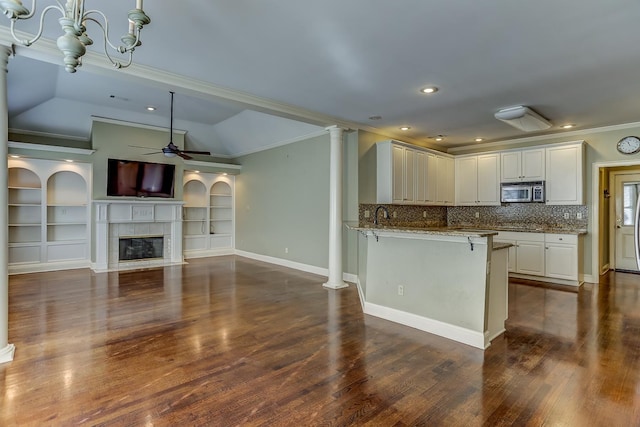 kitchen with kitchen peninsula, a kitchen breakfast bar, light stone counters, vaulted ceiling, and white cabinets