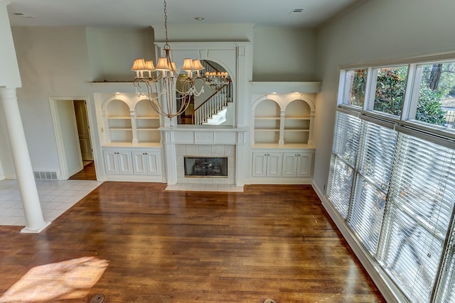 unfurnished living room with a notable chandelier, built in shelves, a tile fireplace, and tile patterned flooring