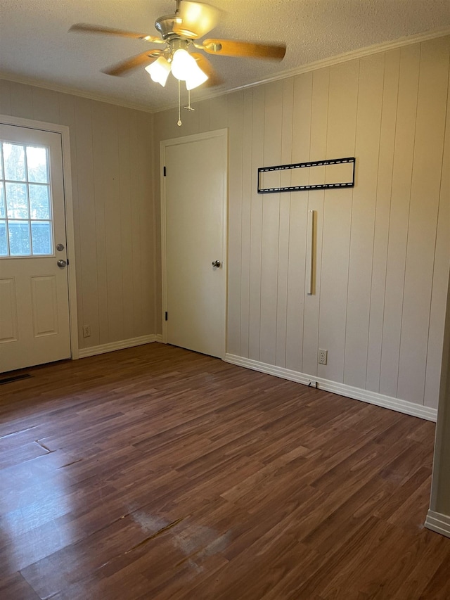 empty room featuring ceiling fan, dark wood-type flooring, crown molding, a textured ceiling, and wooden walls