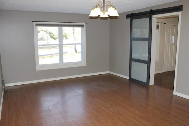 unfurnished room with a chandelier, a textured ceiling, a barn door, and dark wood-type flooring