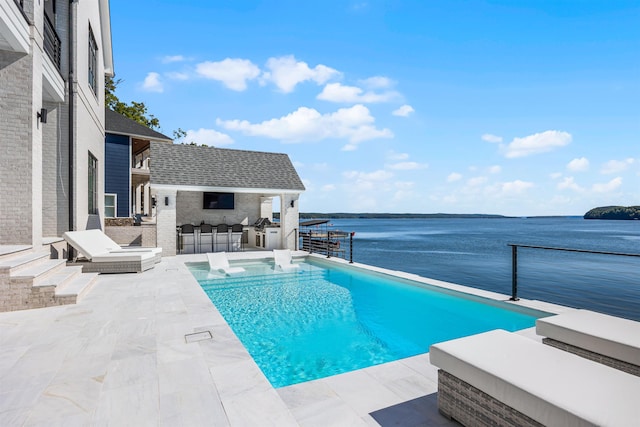 view of swimming pool featuring an outbuilding, a water view, exterior bar, and a patio