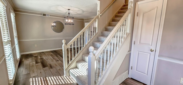 stairs with crown molding, hardwood / wood-style floors, and a notable chandelier