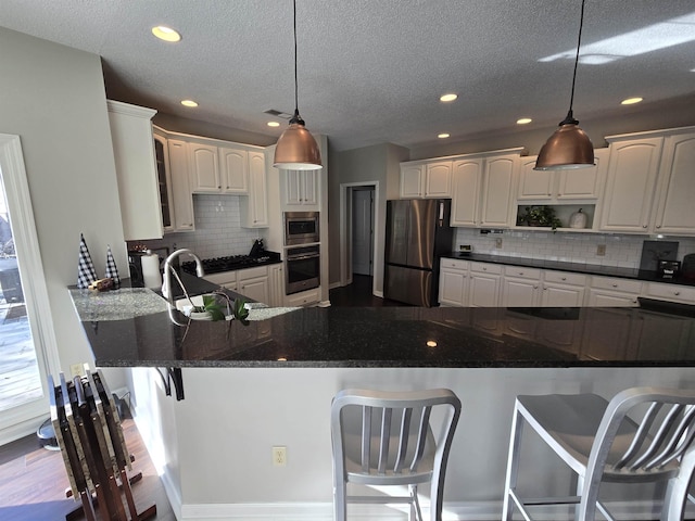 kitchen with kitchen peninsula, appliances with stainless steel finishes, pendant lighting, and a breakfast bar area