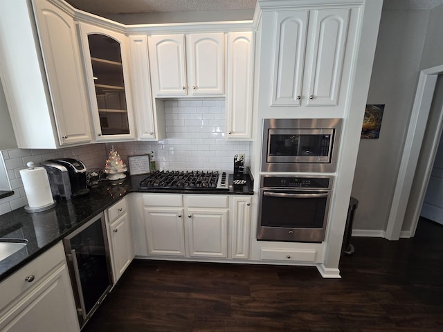 kitchen featuring stainless steel appliances, beverage cooler, dark stone countertops, decorative backsplash, and white cabinets