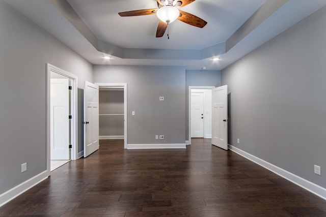 unfurnished bedroom featuring a raised ceiling, ceiling fan, dark hardwood / wood-style flooring, and a closet