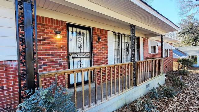 property entrance with crawl space, a porch, and brick siding