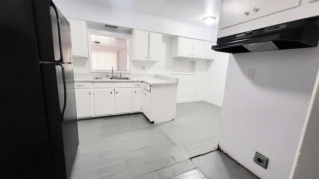 kitchen with under cabinet range hood, a sink, white cabinetry, light countertops, and freestanding refrigerator