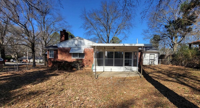 rear view of house featuring brick siding, a chimney, fence, and a sunroom