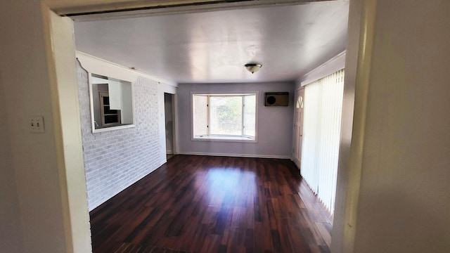 spare room featuring dark wood-style flooring, baseboards, brick wall, and a wall mounted AC