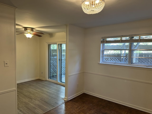 spare room featuring ceiling fan with notable chandelier, dark parquet flooring, ornamental molding, and a wealth of natural light