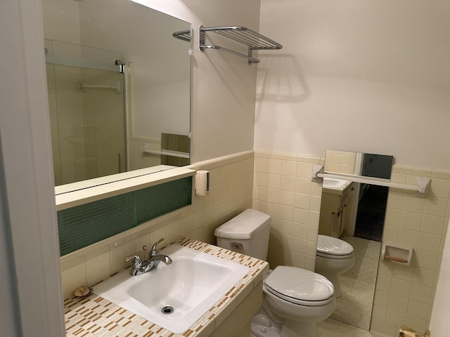 bathroom featuring sink, a shower with door, tile walls, and toilet