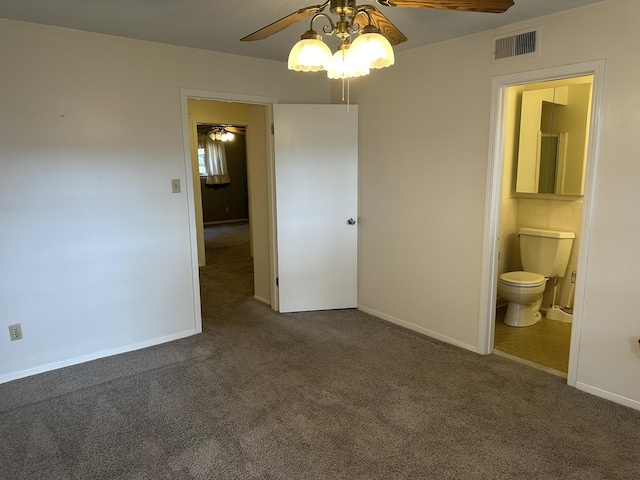 unfurnished bedroom featuring ensuite bathroom, dark carpet, and ceiling fan