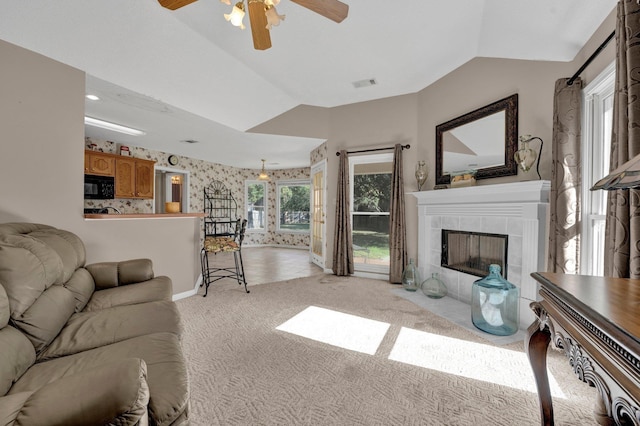 living room featuring a tiled fireplace, ceiling fan, light carpet, and lofted ceiling