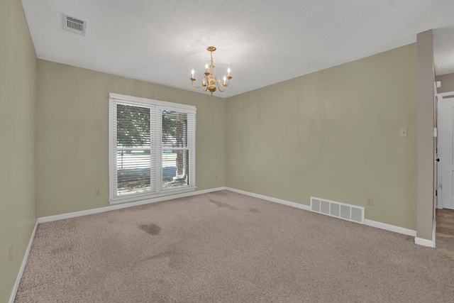 spare room featuring a chandelier, a textured ceiling, and carpet flooring