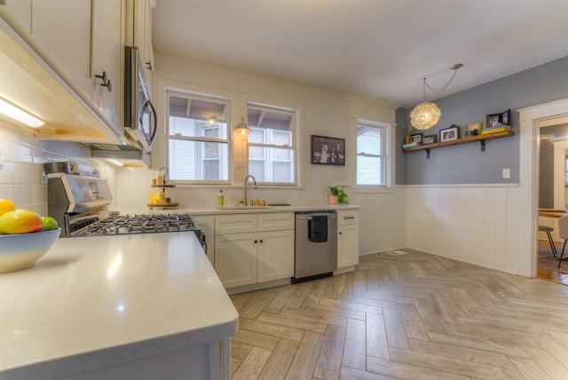 kitchen featuring sink, appliances with stainless steel finishes, decorative light fixtures, white cabinetry, and light parquet flooring