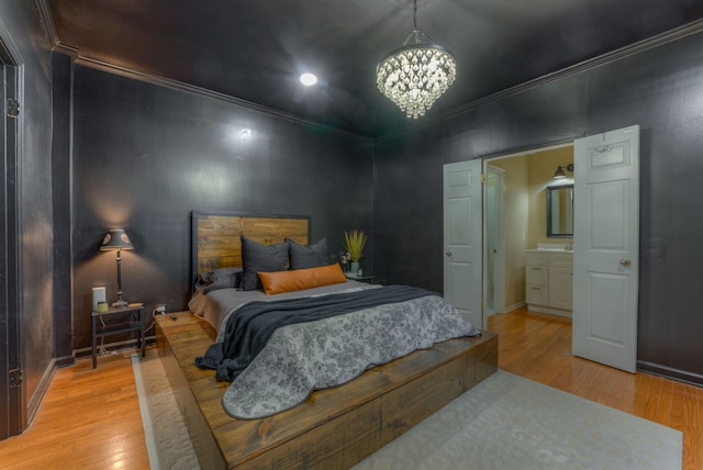 bedroom with a notable chandelier, light hardwood / wood-style floors, ornamental molding, and connected bathroom