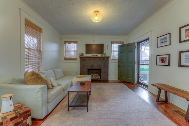 living room featuring a brick fireplace, ornamental molding, a textured ceiling, and light hardwood / wood-style flooring