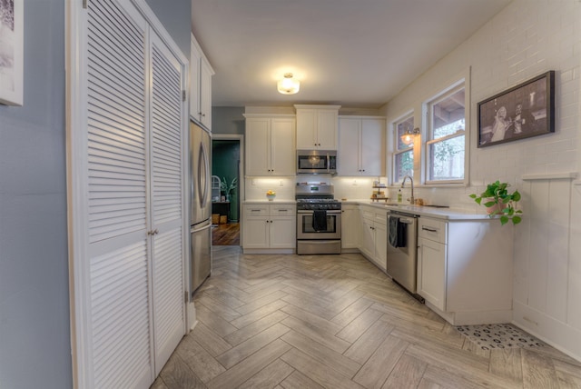 kitchen with light parquet floors, sink, decorative backsplash, appliances with stainless steel finishes, and white cabinetry