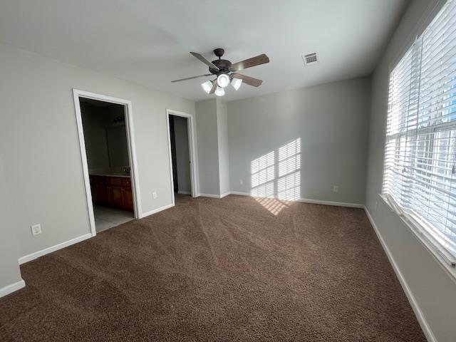 unfurnished bedroom with carpet flooring, connected bathroom, multiple windows, and ceiling fan