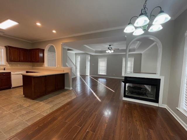 kitchen with a multi sided fireplace, dark hardwood / wood-style flooring, white dishwasher, ceiling fan with notable chandelier, and ornamental molding