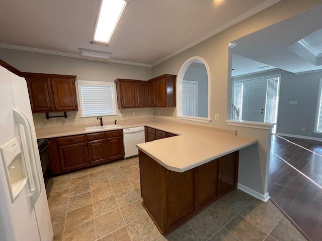 kitchen with crown molding, white appliances, kitchen peninsula, and sink