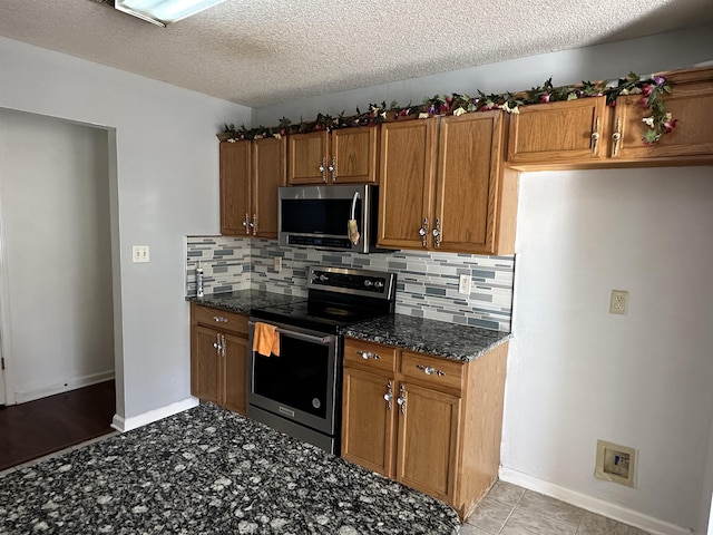 kitchen with backsplash, dark stone counters, stainless steel appliances, and a textured ceiling