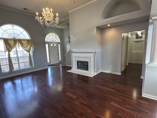 unfurnished living room with dark hardwood / wood-style floors, crown molding, a tile fireplace, and a chandelier