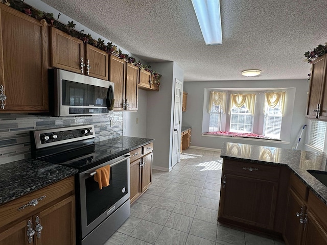 kitchen featuring appliances with stainless steel finishes, backsplash, dark stone countertops, and light tile patterned flooring