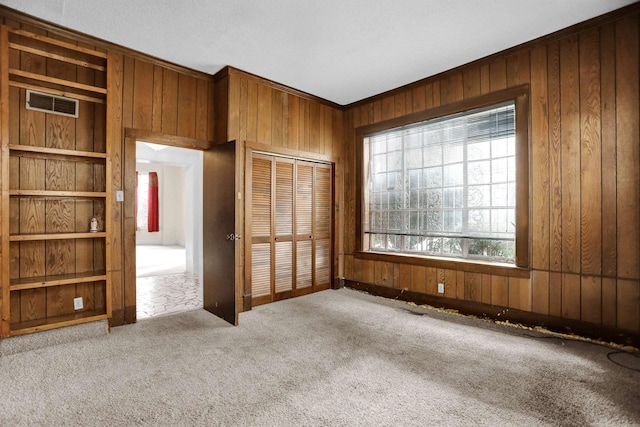 unfurnished bedroom featuring carpet flooring, wood walls, and a closet