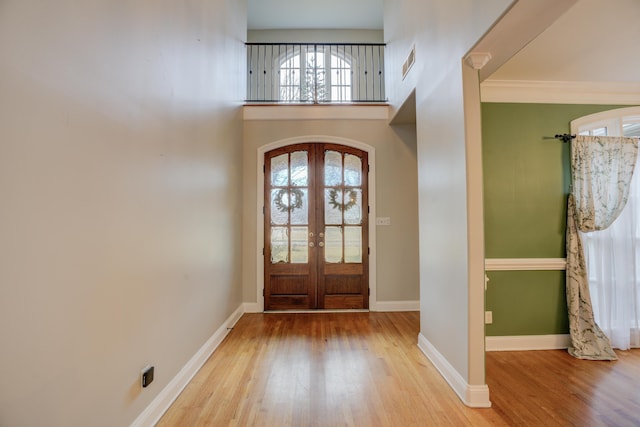 foyer entrance featuring light hardwood / wood-style floors, ornamental molding, a towering ceiling, and french doors