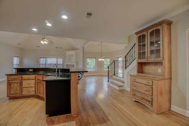 kitchen featuring a breakfast bar, sink, pendant lighting, dark stone counters, and light hardwood / wood-style floors