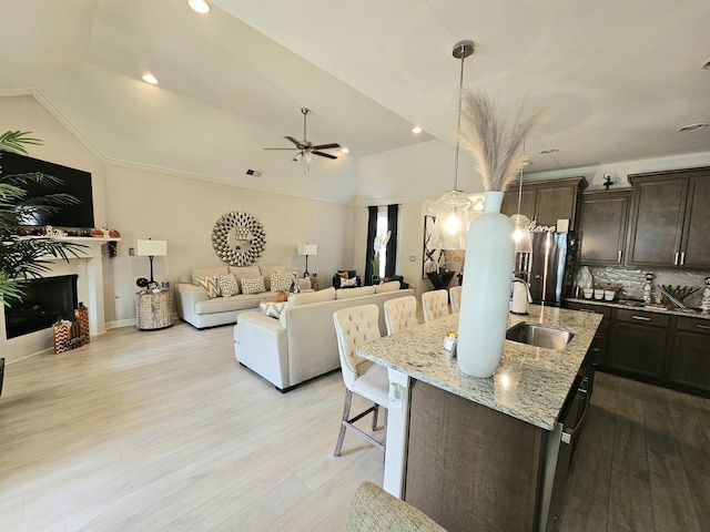 kitchen featuring a kitchen bar, dark brown cabinets, a kitchen island with sink, sink, and lofted ceiling