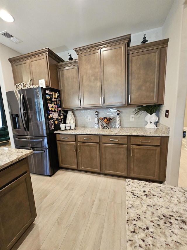 kitchen featuring light hardwood / wood-style floors, dark brown cabinetry, light stone countertops, and stainless steel refrigerator with ice dispenser