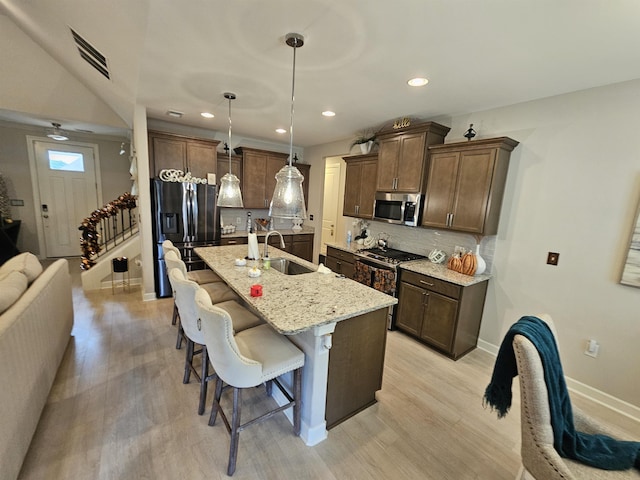 kitchen with sink, hanging light fixtures, backsplash, an island with sink, and appliances with stainless steel finishes